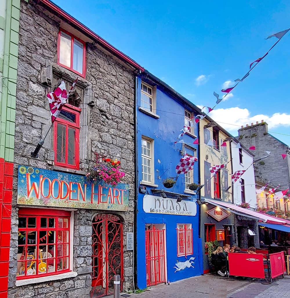 Colourful shopfronts on Quay Street, Galway city with bunting, cafés and traditional stone buildings.