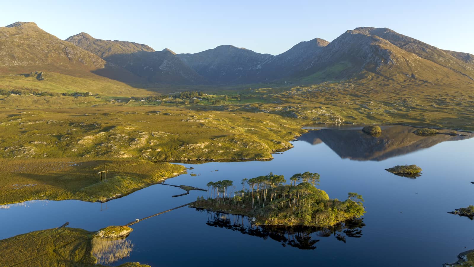 Derryclare Lough in Connemara, County Galway, with small wooded island, mountains and reflections in calm water.