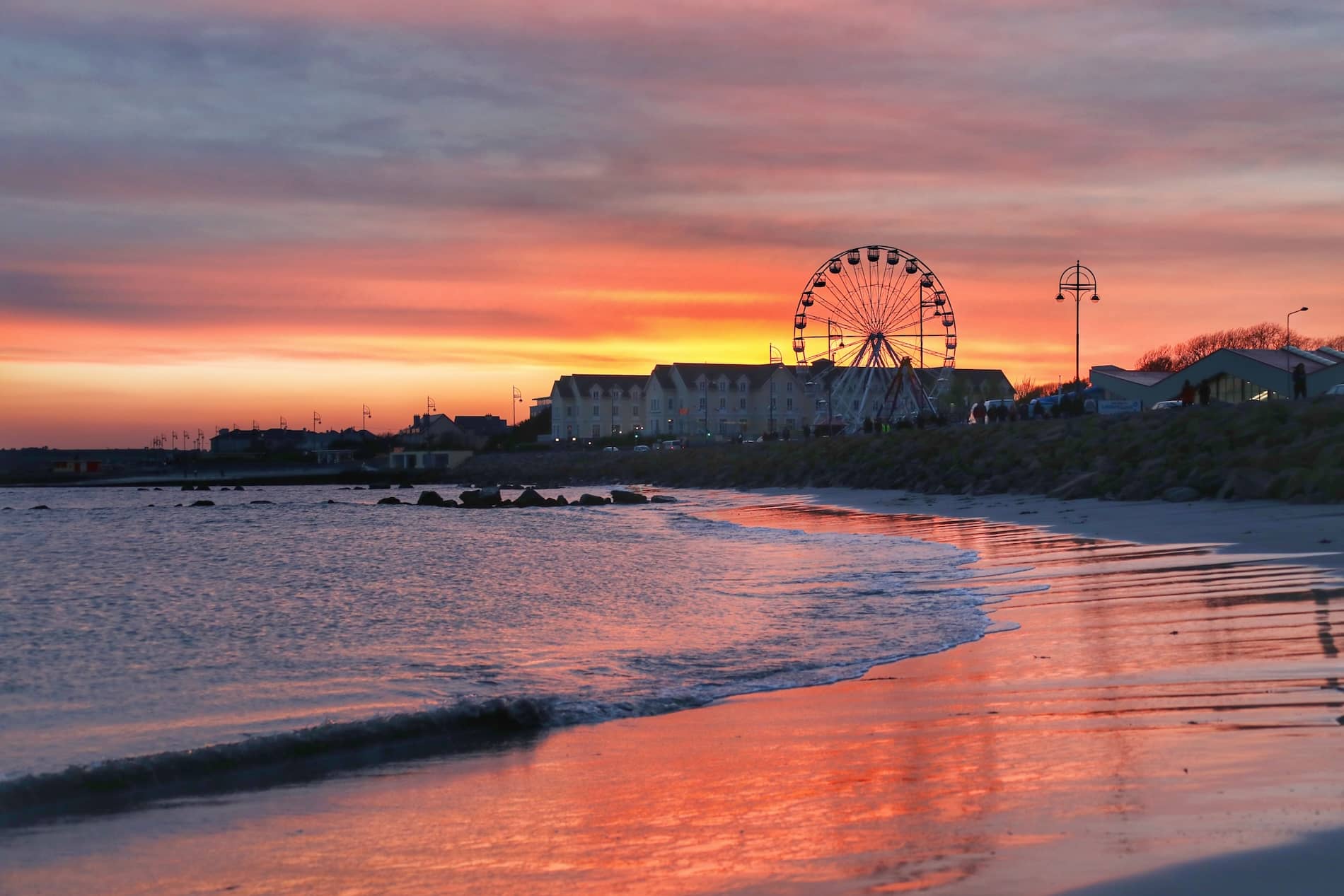 Ferris wheel beside Salthill beach at sunset with colourful skies reflected on the shoreline in Galway.