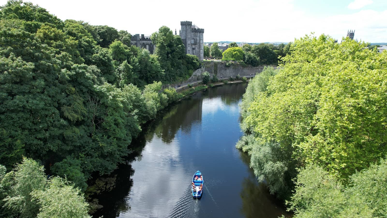 Boat trip on the River Nore with Kilkenny Castle and leafy banks in view.