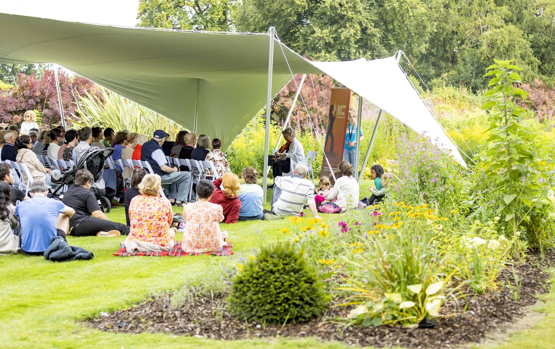 Audience enjoying live music at Kilkenny Arts Festival in a garden setting under a canopy.