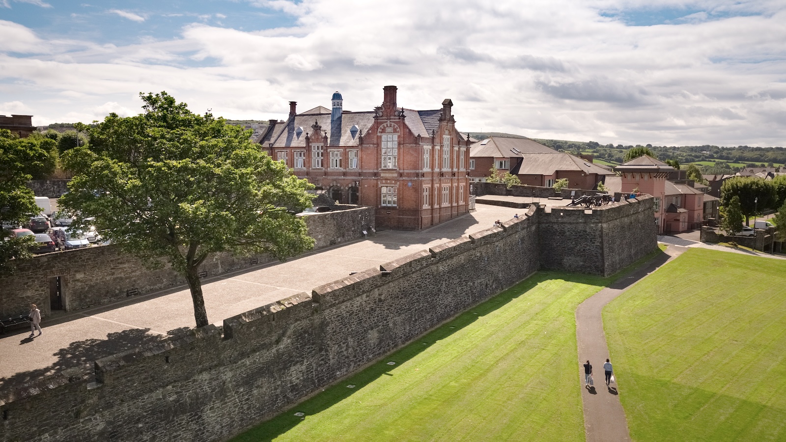 People walking along Derry~Londonderry city walls with green space and heritage buildings.