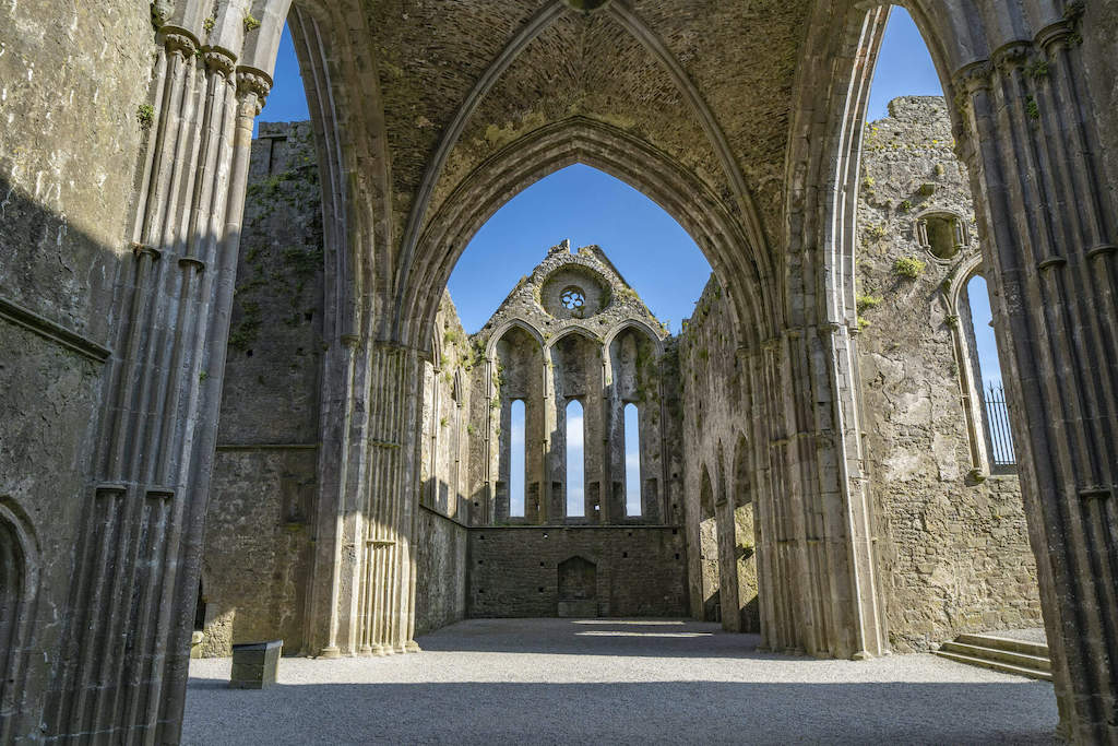 Interior view of the Rock of Cashel ruins in County Tipperary, showing Gothic arches and stone walls in sunlight.