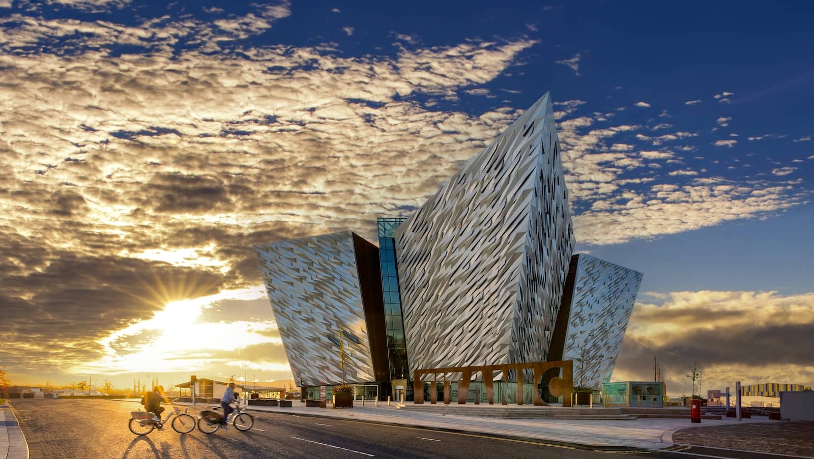 Titanic Belfast at sunset, with cyclists passing along the waterfront in Belfast’s Titanic Quarter.