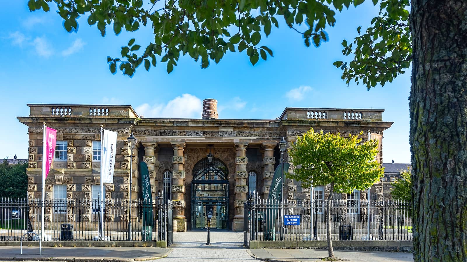 Crumlin Road Gaol in Belfast, with its grand stone entrance and iron railings under blue skies.