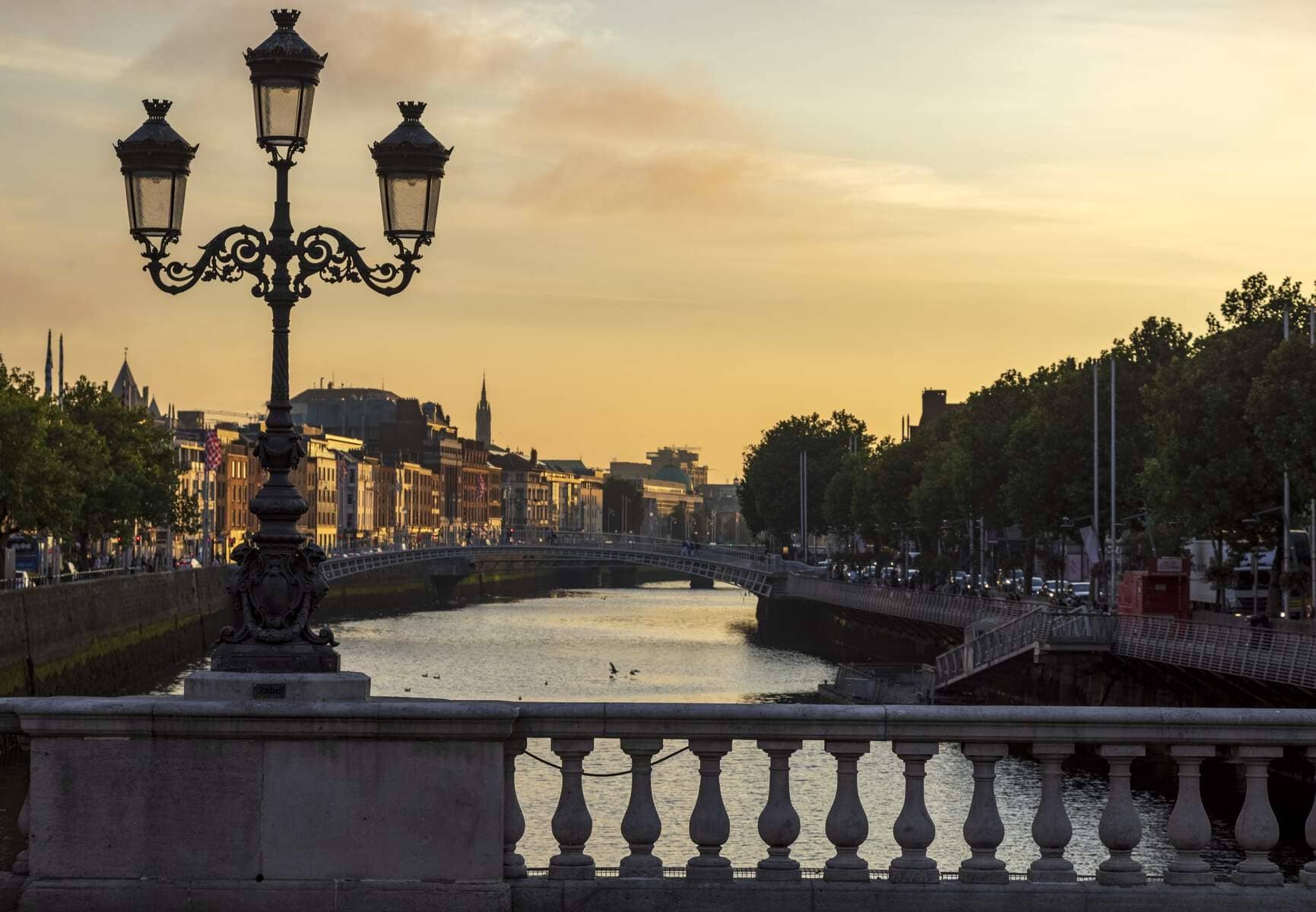 View of O'Connell Bridge and city skyline lit by golden evening light over the River Liffey.