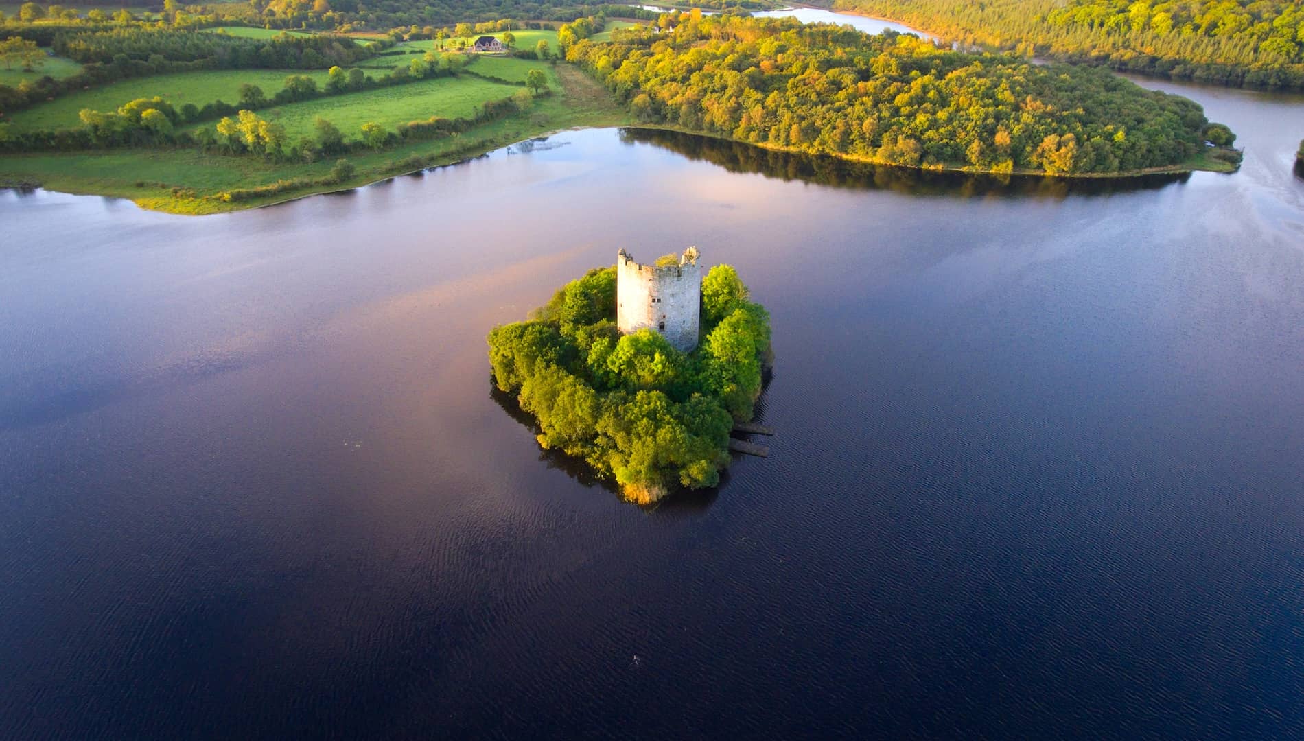 Aerial view of Cloughoughter Castle on a wooded island in Lough Oughter, County Cavan, surrounded by calm water.