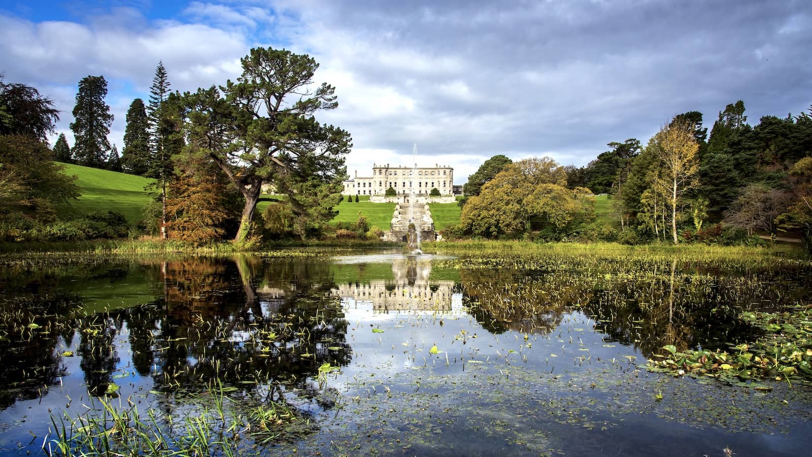 Powerscourt House in County Wicklow overlooking landscaped gardens and lake, framed by mature trees and rolling lawns.