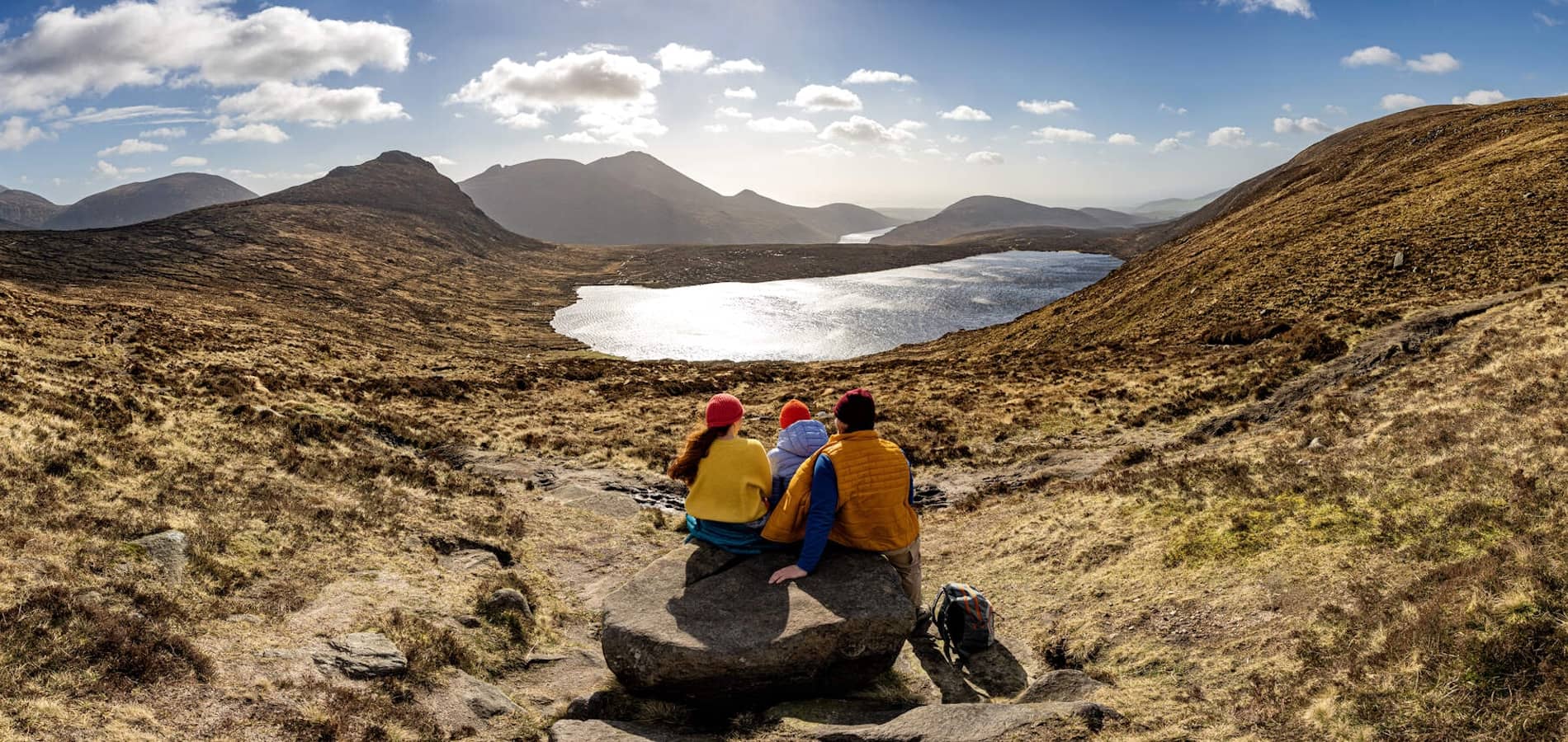 Hikers resting on Mourne Way trail with panoramic view of lakes and Mourne Mountains in County Down, Northern Ireland.