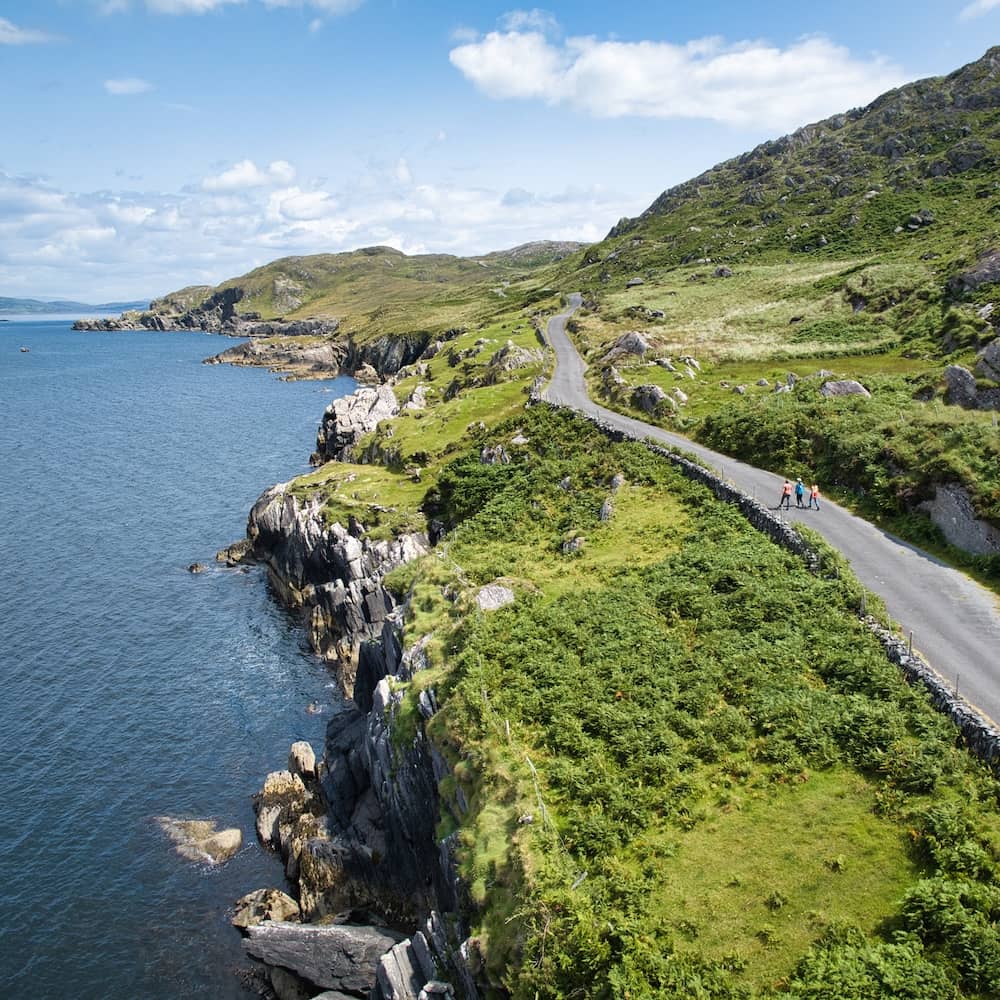 Scenic coastal road on the Beara Peninsula, County Cork, with walkers enjoying sea views and rugged green hills.
