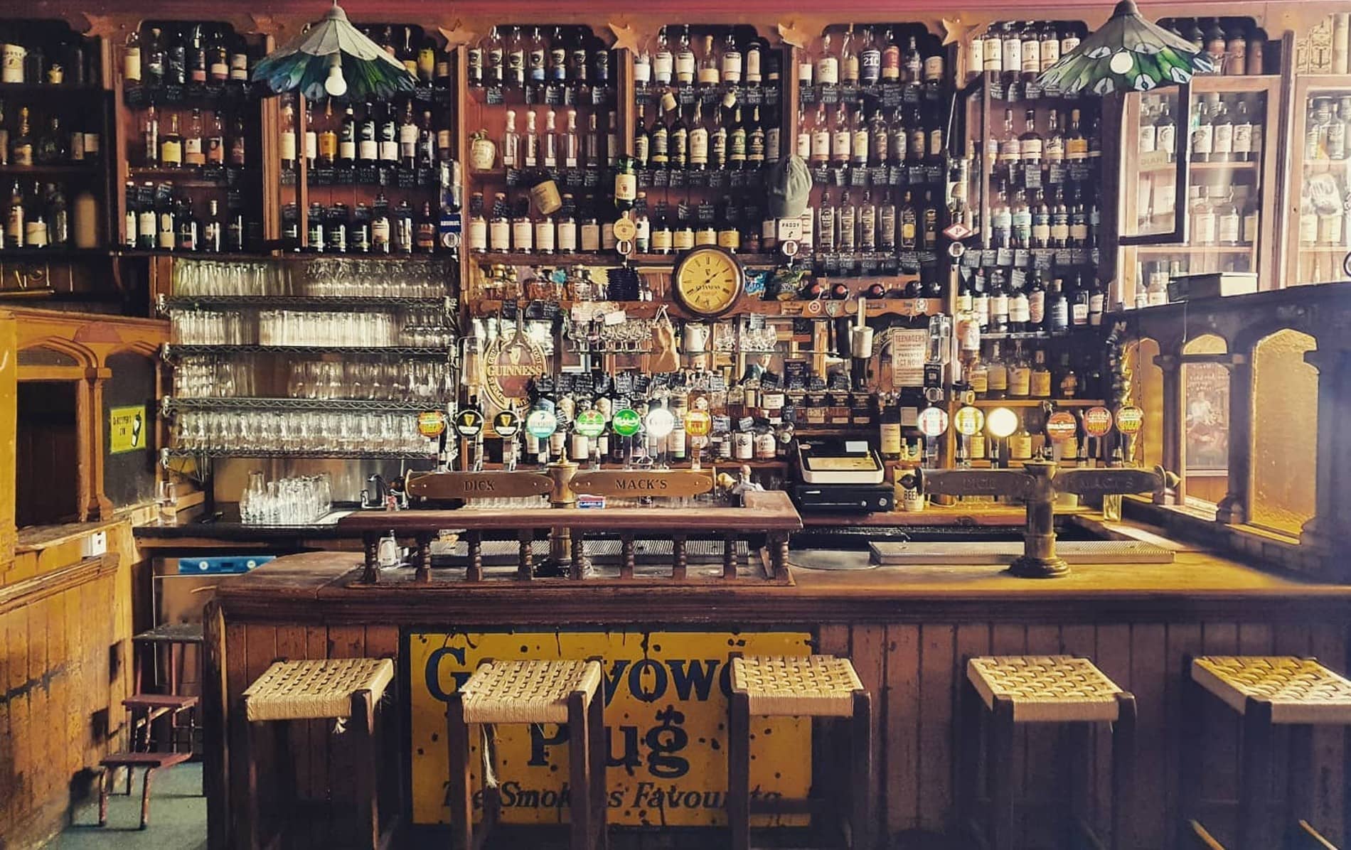 Wood-panelled bar at Dick Mack’s pub in Dingle, County Kerry, with shelves of bottles and glasses.