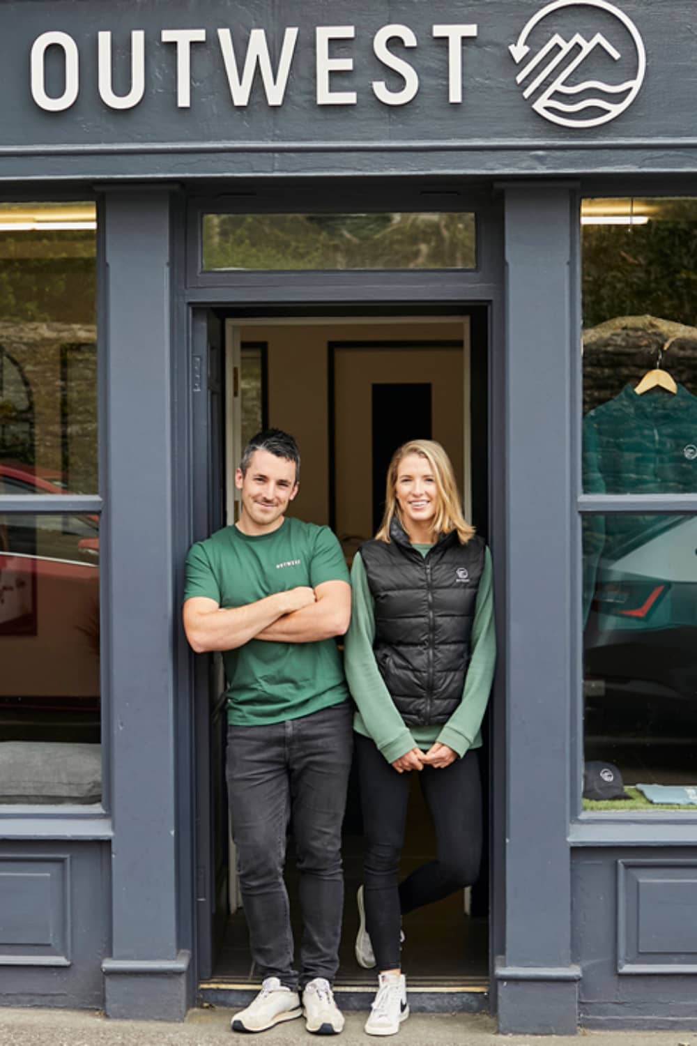 Two people stand at the entrance of Outwest shop in Dingle, County Kerry, smiling at the doorway.
