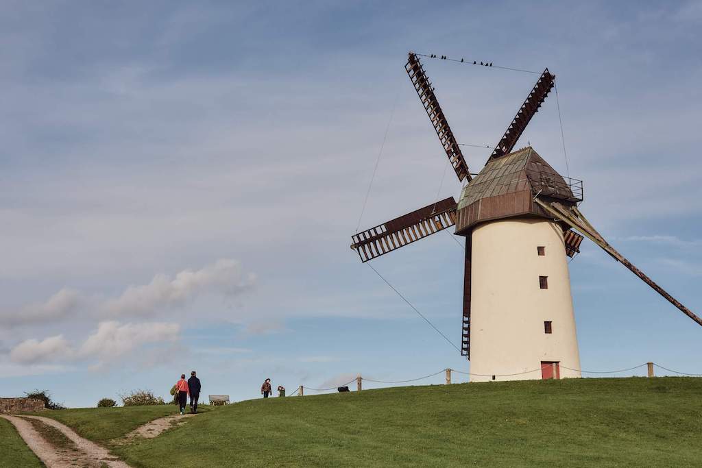 People walk a grassy hill past the historic Skerries Windmill under a soft blue sky with light cloud cover.