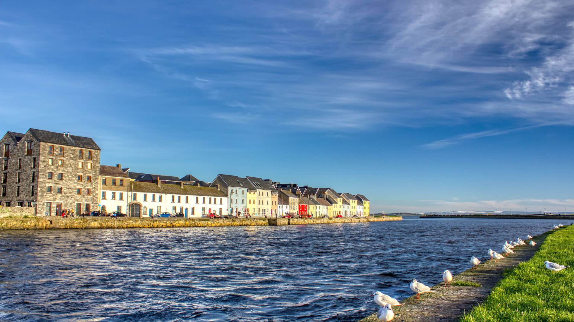 Colourful houses along the Claddagh Quay waterfront in Galway City under a bright blue sky.