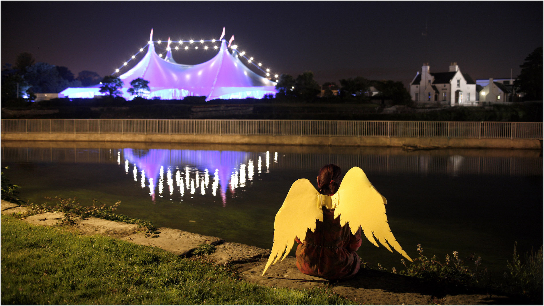 Night view of Galway International Arts Festival tent lit in purple, reflected in the River Corrib.