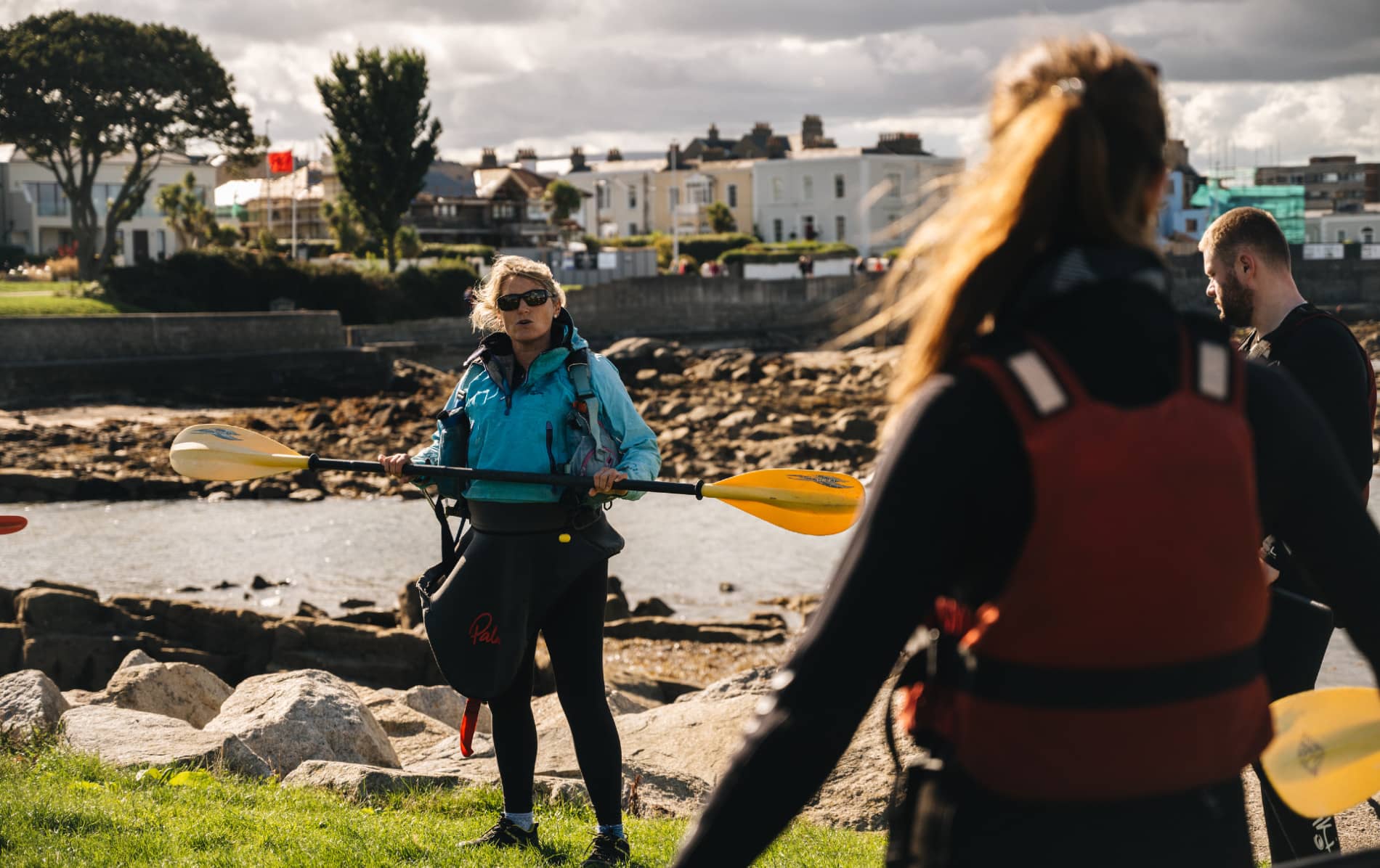 Instructor demonstrating paddle technique to kayakers wearing life jackets on the shore near Dalkey, Dublin.