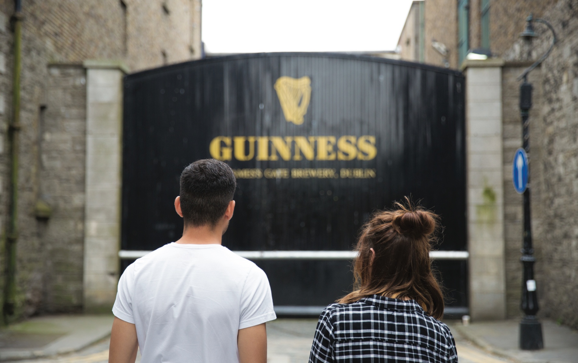 Two visitors facing the iconic black gates at the Guinness Storehouse in Dublin.