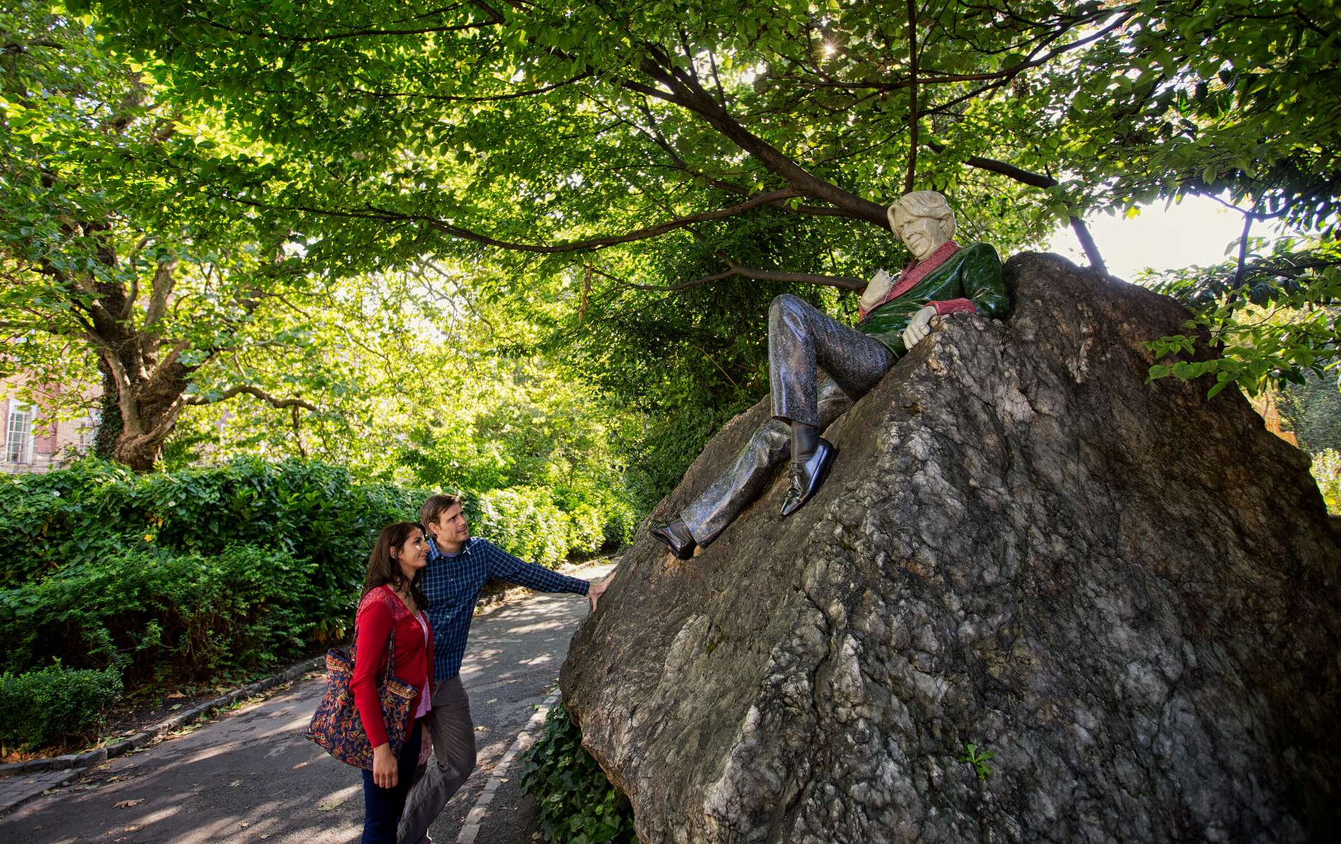 Couple admiring the Oscar Wilde statue on a large rock in Dublin’s Merrion Square Park.