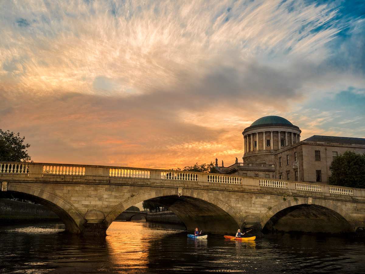 Two kayakers on the River Liffey with the Four Courts in Dublin at sunset.
