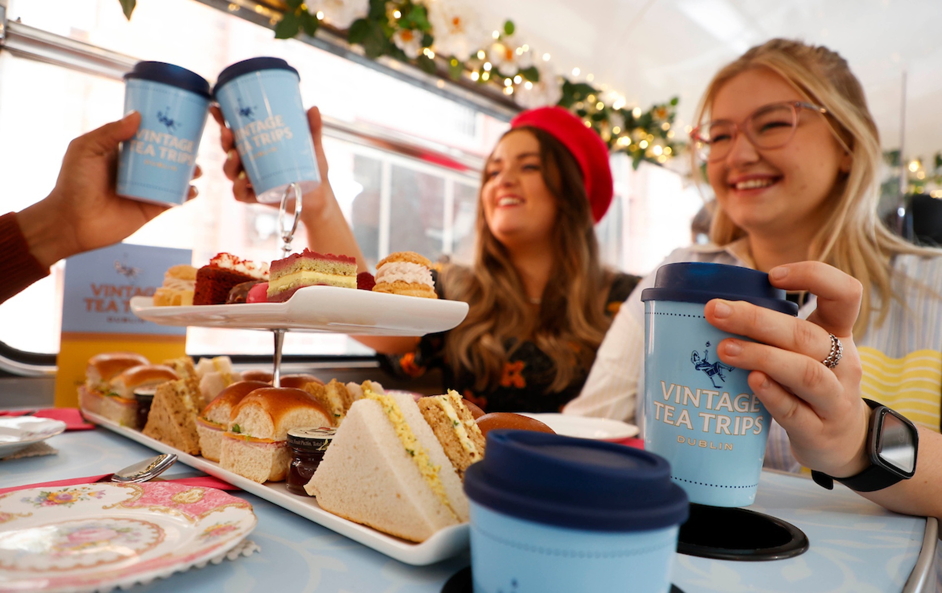 Friends enjoying afternoon tea with cakes on the Vintage Tea Trips bus in Dublin.