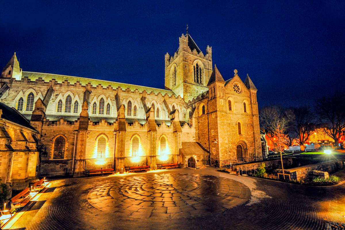 Christ Church Cathedral in Dublin illuminated at night against a dark blue sky.