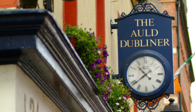 The Auld Dubliner sign with a vintage-style clock hanging over the entrance, surrounded by flowers in Temple Bar, Dublin.