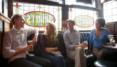 Four friends sitting inside O’Neill’s Pub on Suffolk Street, Dublin, with stained-glass windows behind them reading ‘Spirits’.