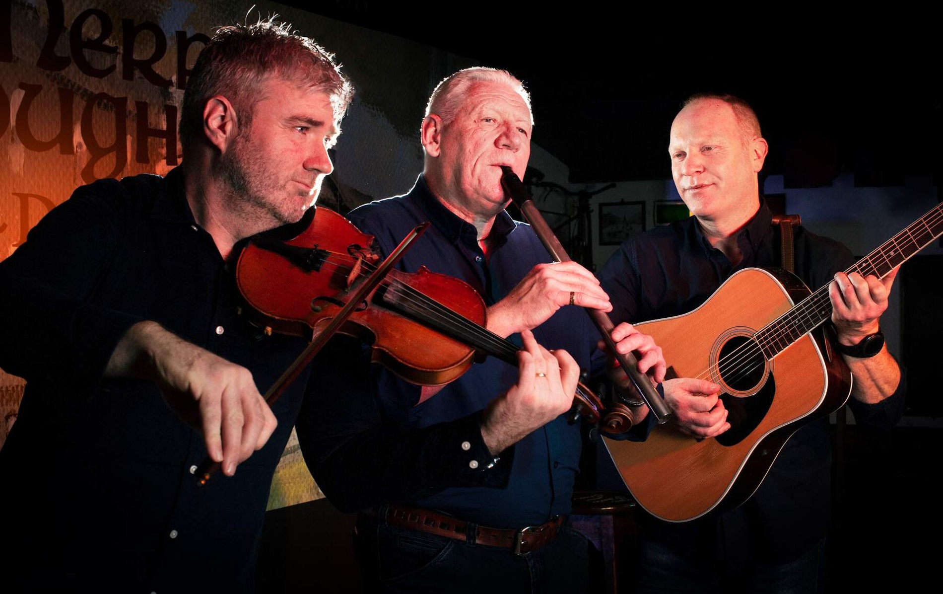 Three traditional musicians playing fiddle, flute, and guitar in a moody pub setting, representing top trad music pubs in Dublin.