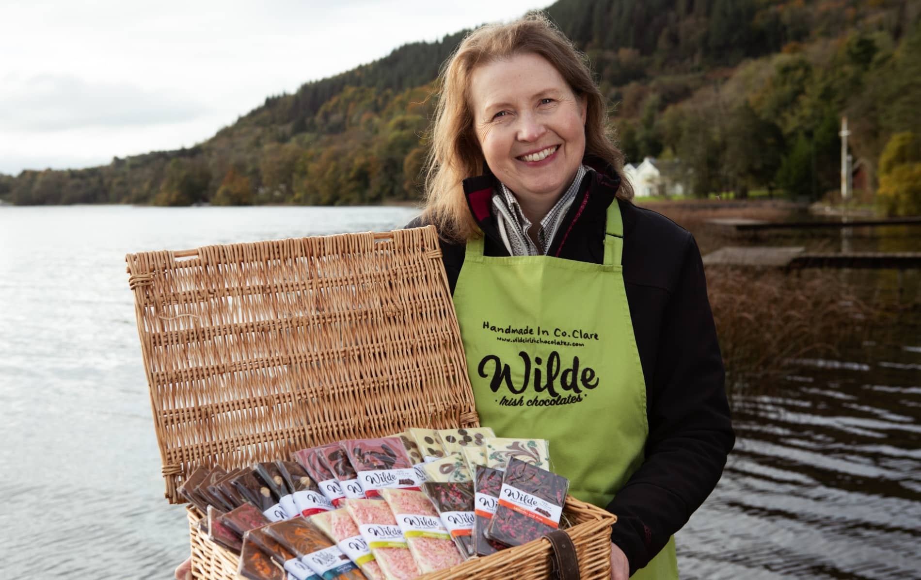 Smiling woman with basket of Wilde Irish Chocolates by a lakeside in County Clare.