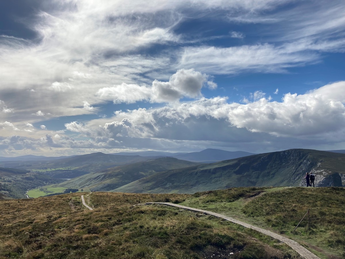 Two walkers standing on a wooden trail in Wicklow Mountains National Park with valley views.