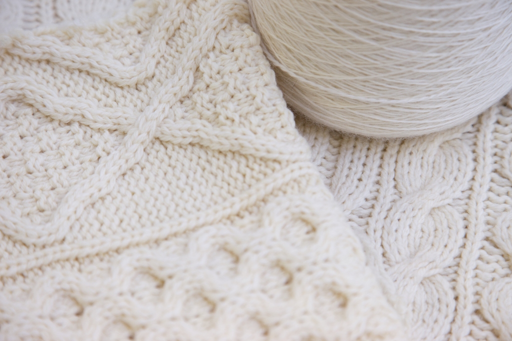 Traditional Aran knit patterns in undyed wool showcased alongside a spool of yarn – a celebration of Galway’s craft heritage.