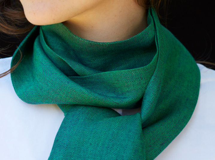 A close-up of an elegant electric green herringbone linen scarf from Stable of Ireland, gracefully tied at the neck.