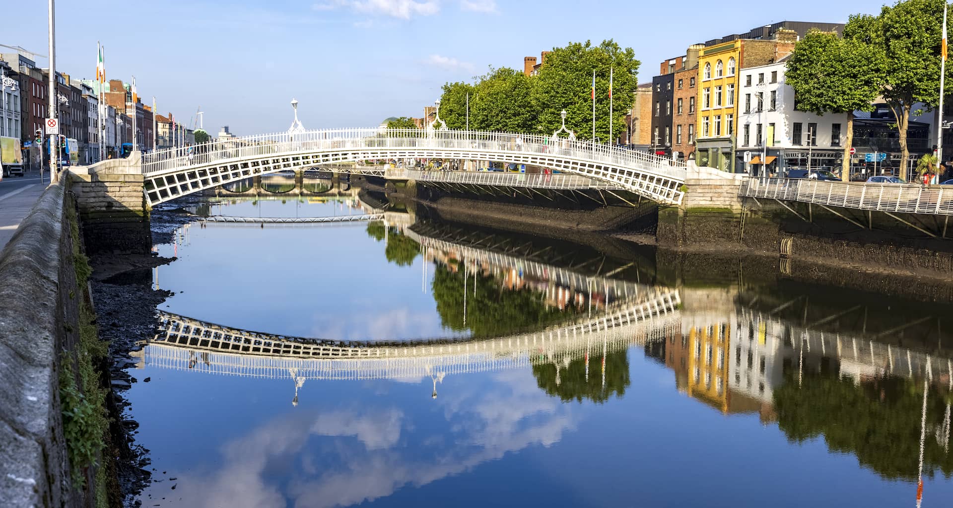 Morning sunlight reflecting off the Ha’penny Bridge and colourful riverside buildings on the River Liffey in Dublin.