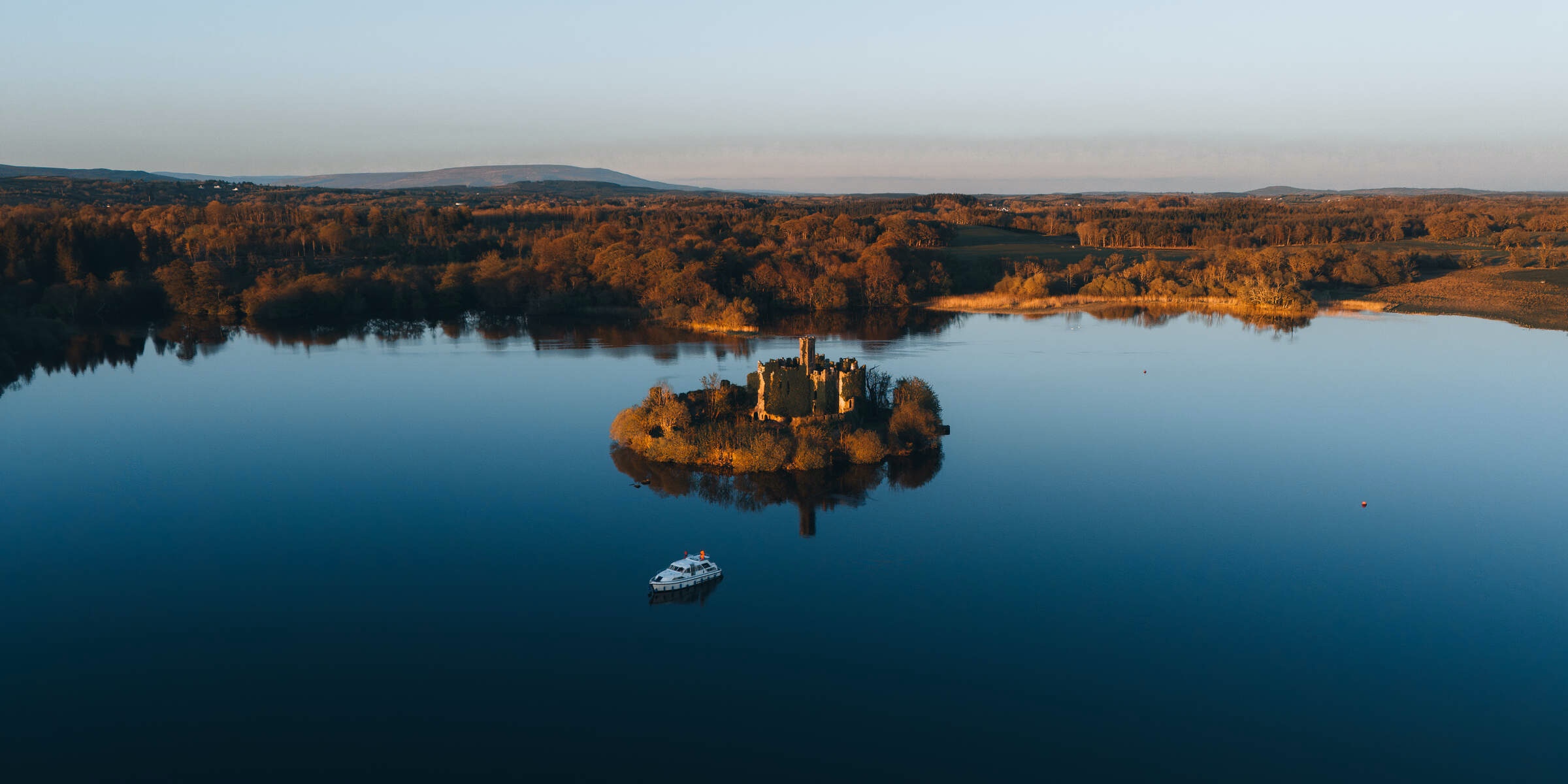 Autumn trees line the banks of a quiet lake, with a wooded island and a boat below.