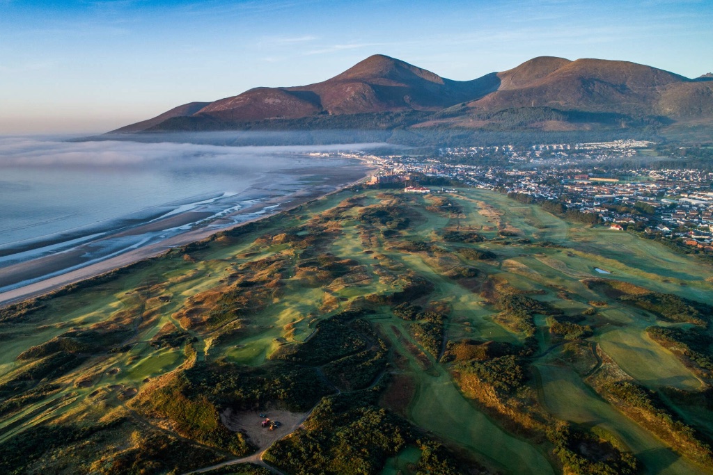 Aerial view of a lush golf course stretching to the coastline, with the Mourne Mountains in the distance.