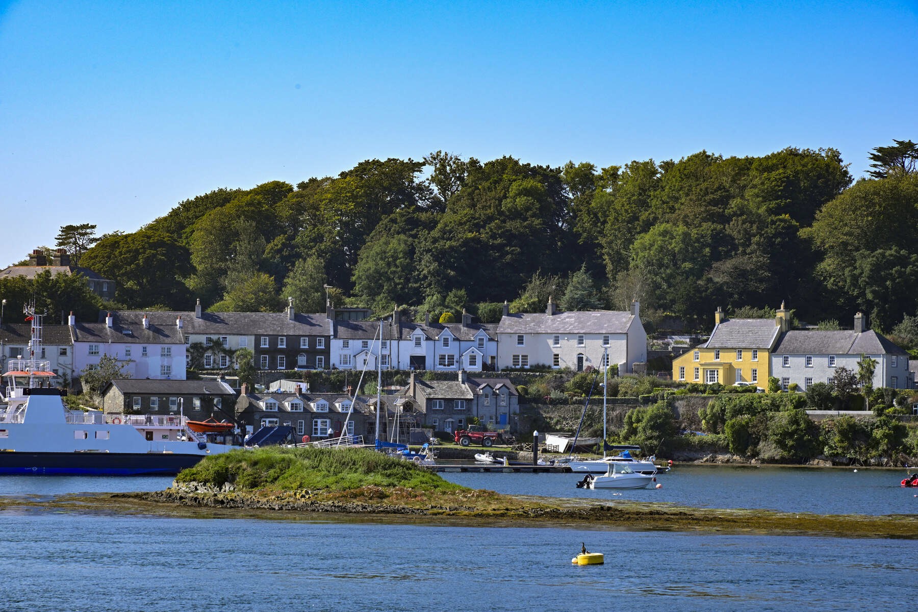 Colourful houses line the edge of a wooded shoreline beside calm waters and clear blue skies.