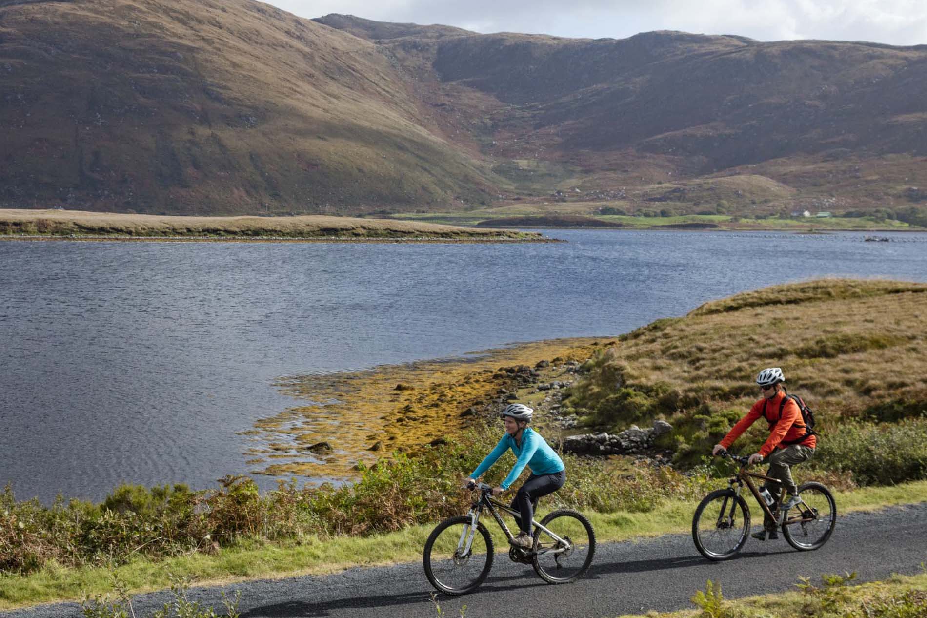 Two cyclists riding the Great Western Greenway, County Mayo, with mountains rising behind.