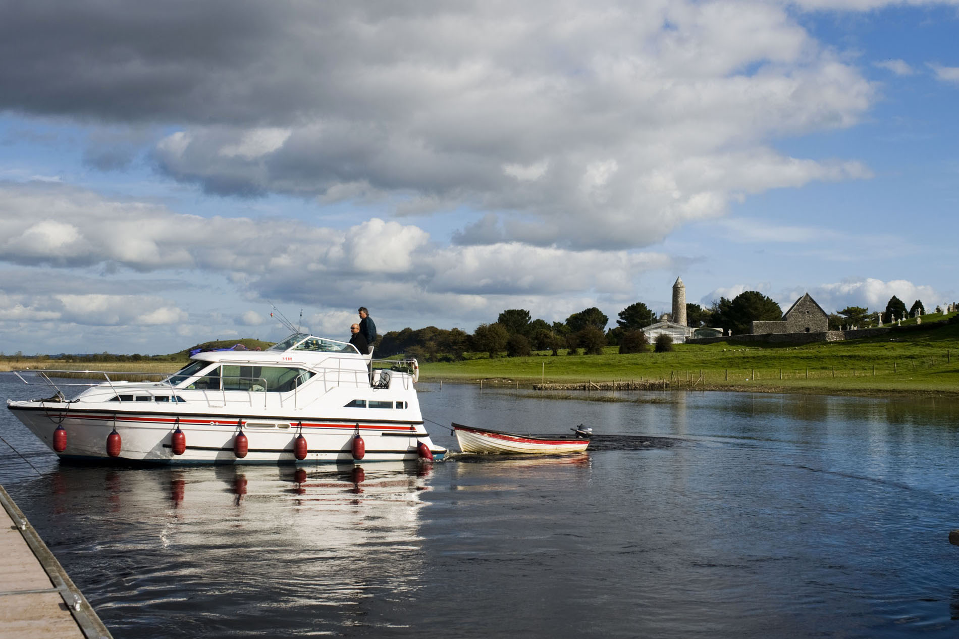 Boat cruising on the River Shannon near Clonmacnoise monastic site with round tower in the distance.