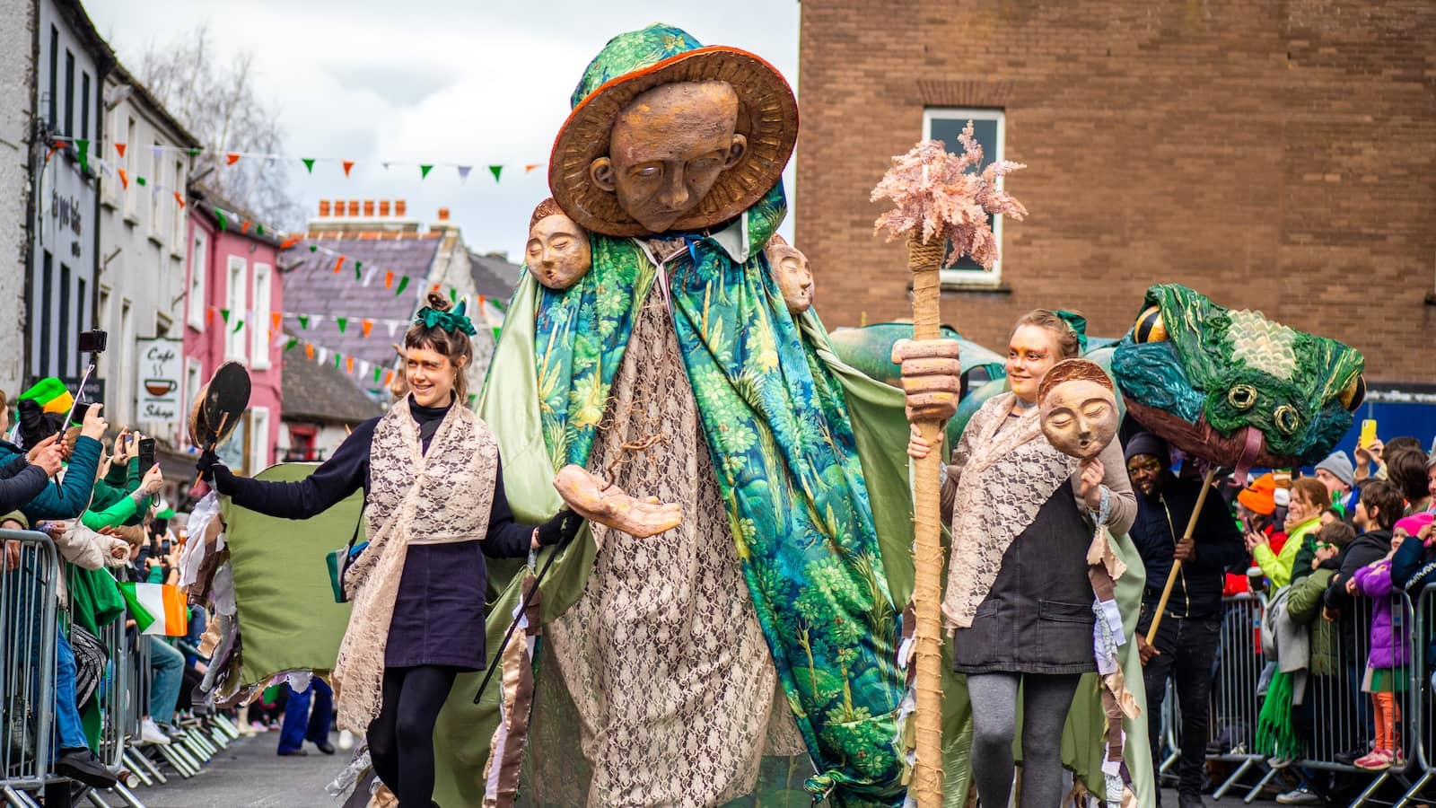 Giant green-cloaked figure leads St Patrick’s Day parade through Kilkenny streets lined with spectators.