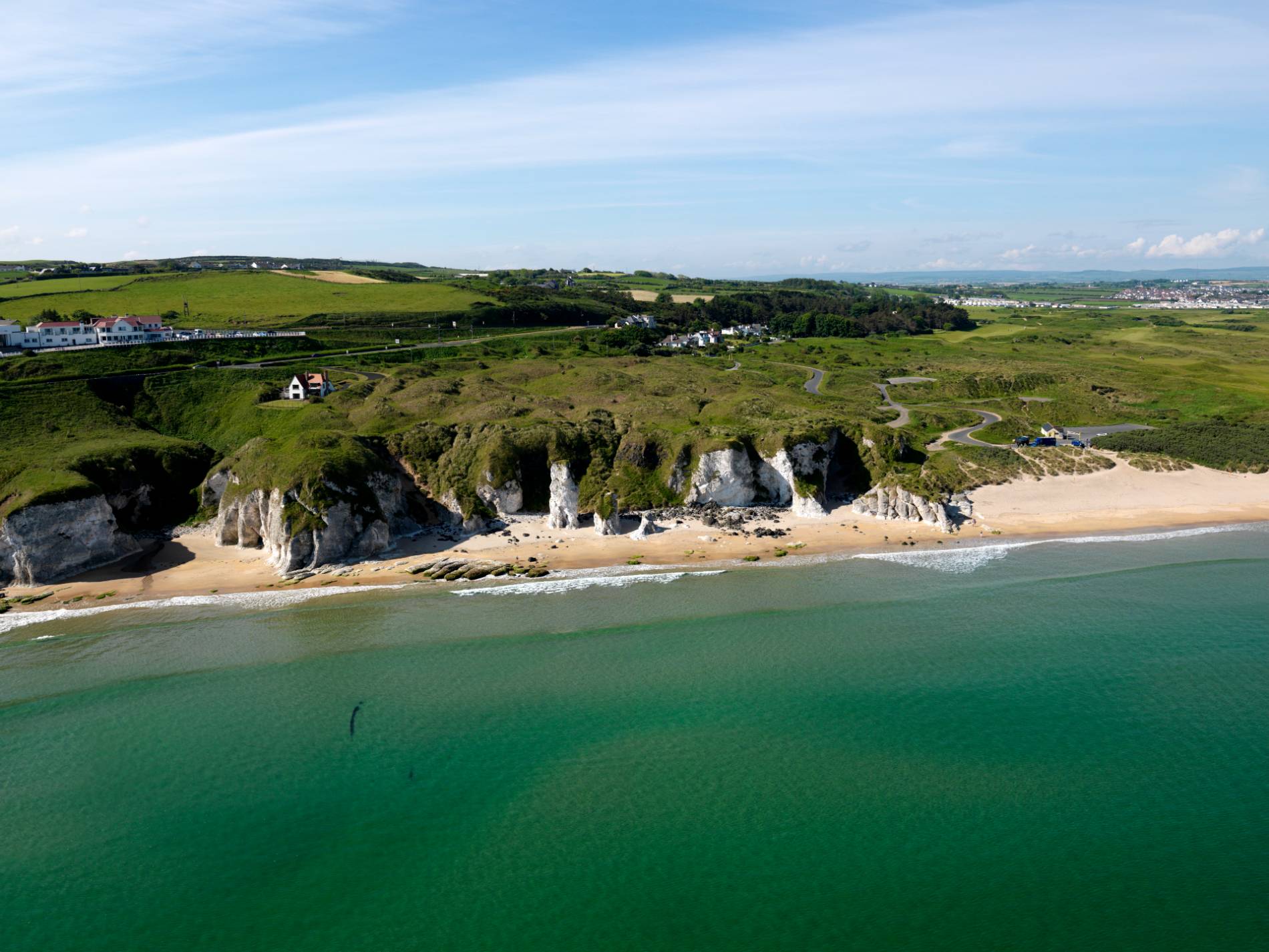 White sandy beach backed by cliffs near Portrush in County Antrim with walking trails leading along the coastline.