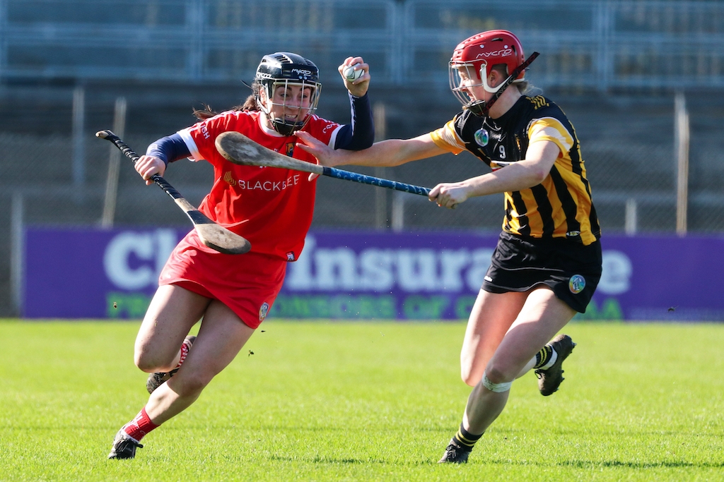 Intense camogie match with players in red and black-and-amber jerseys competing for the sliotar.