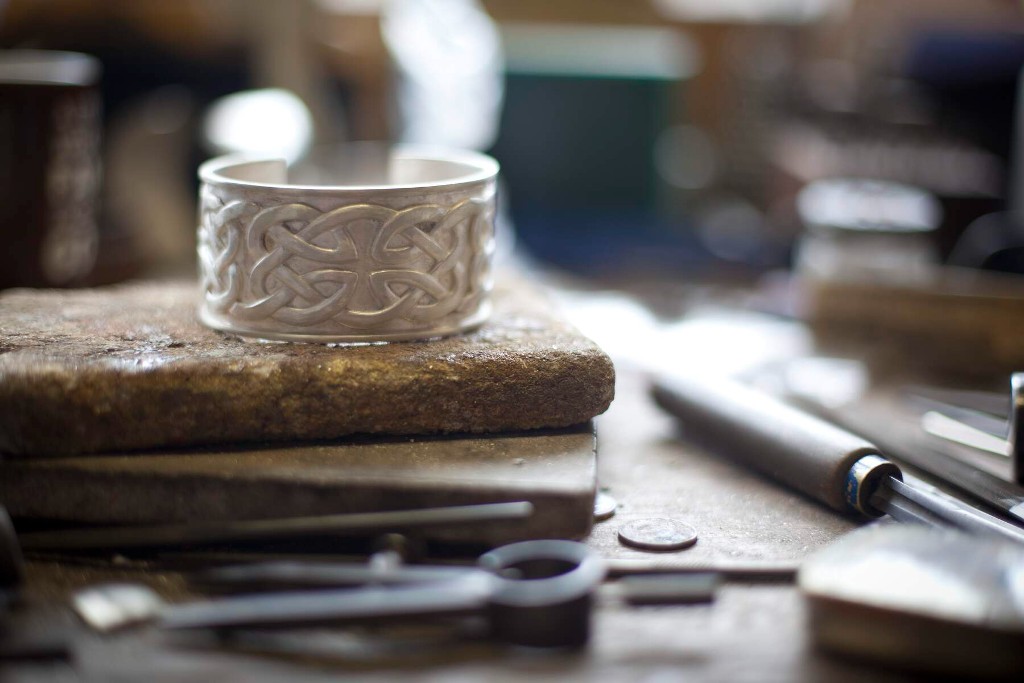 Close-up of handcrafted silver ring with Celtic knot design on a jeweller’s workbench in Kilkenny Design Centre.