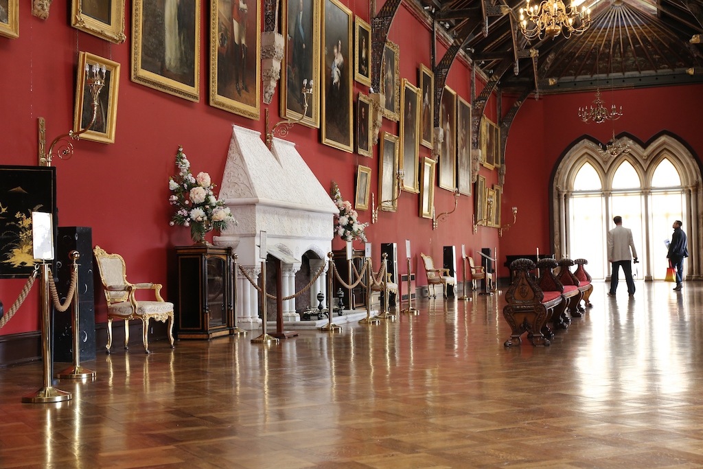 Ornate Long Gallery inside Kilkenny Castle with red walls, portraits, chandeliers and wooden floor.