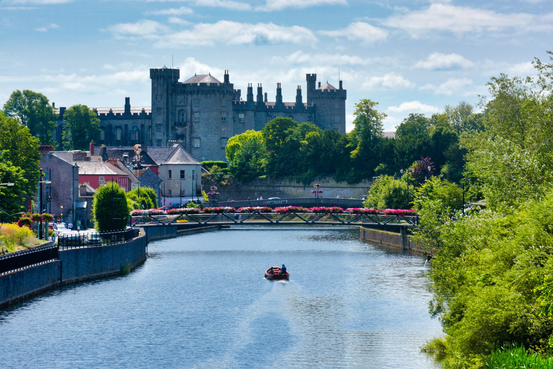 Kilkenny Castle overlooking the River Nore with floral bridge and people boating in Kilkenny City.