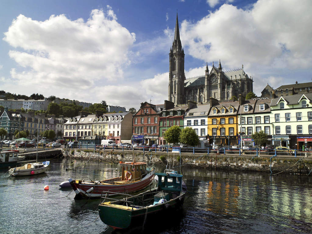 Boats moored at Cobh harbour with colourful houses and St Colman’s Cathedral in the background.