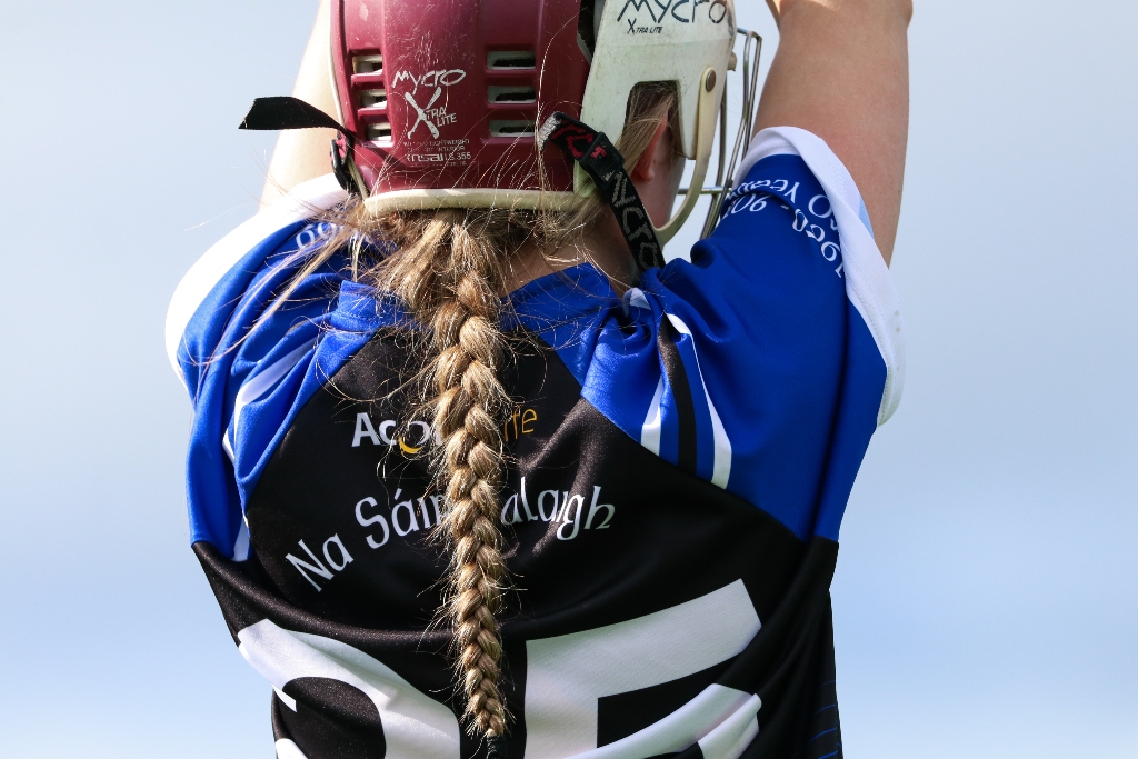 Camogie player from Na Sáirséalaigh club in helmet and jersey prepares to strike during a semi-final match in Cork.