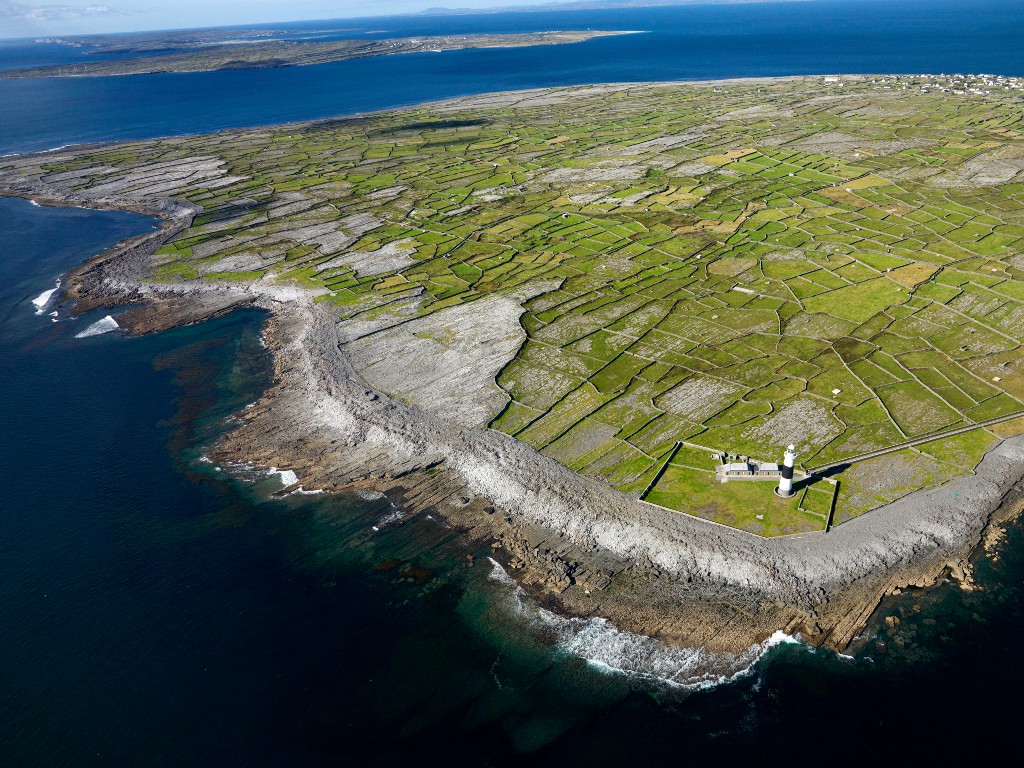 Aerial view of Aran Islands coastline with patchwork stone-walled fields and lighthouse near the shore.