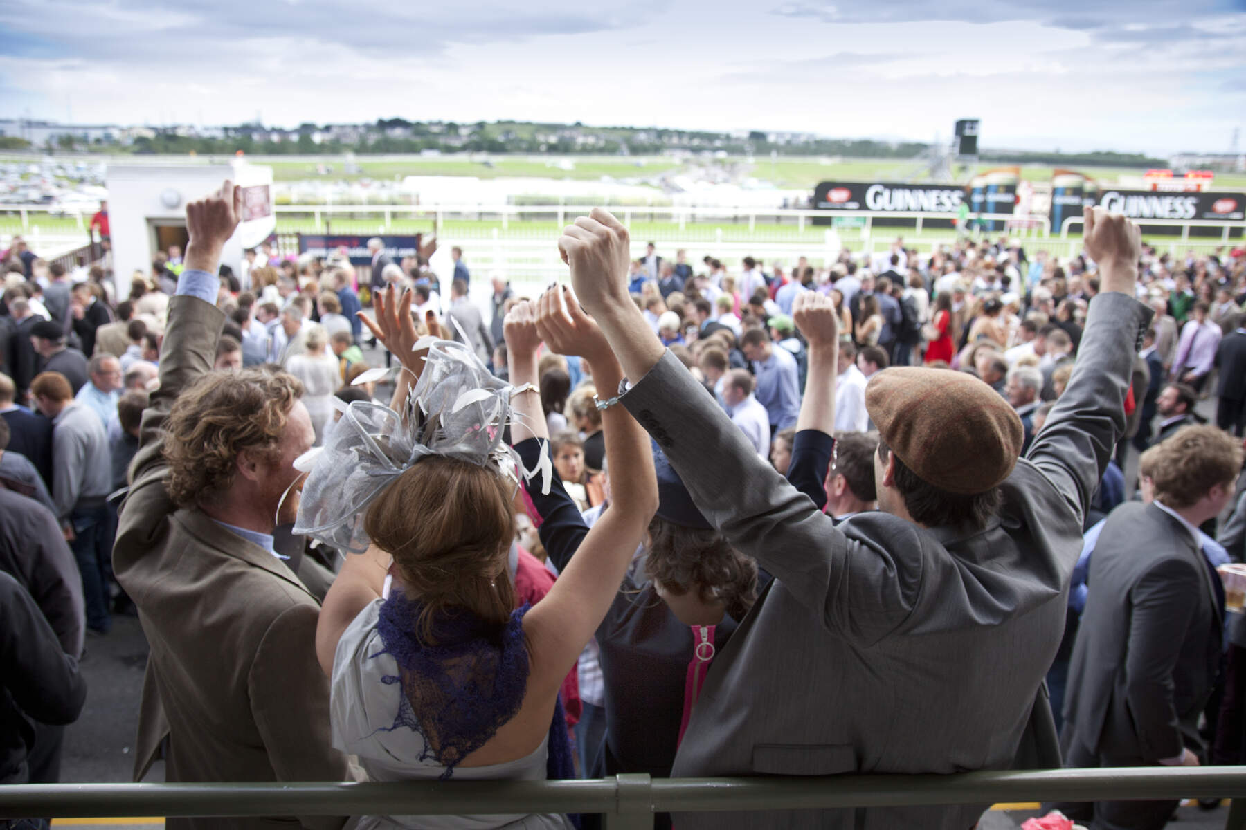 Excited racegoers cheer from the stands at Galway Races, overlooking the busy track and crowds.