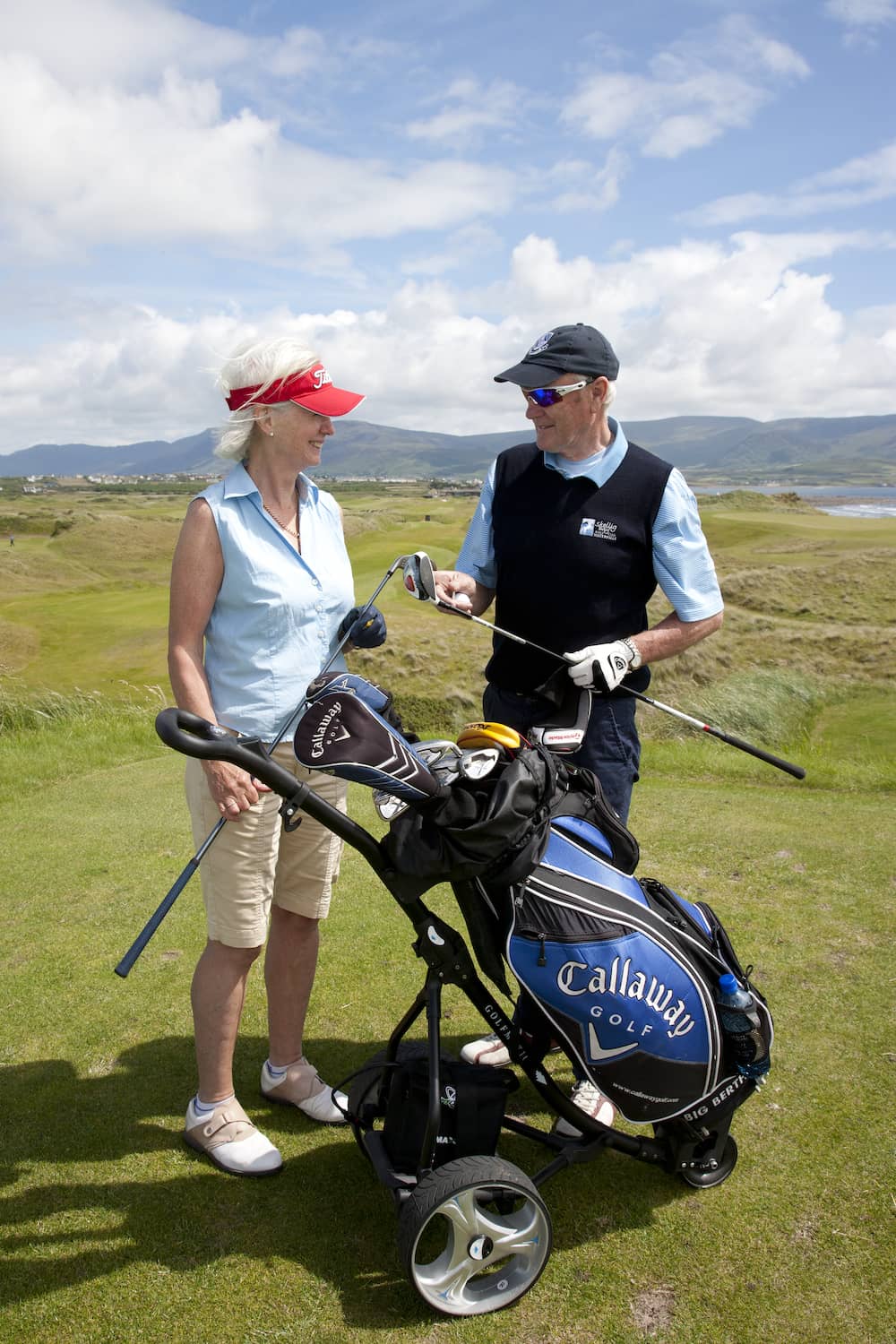 Two golfers chatting beside a golf bag at Waterville Golf Course in County Kerry with mountains in the background.