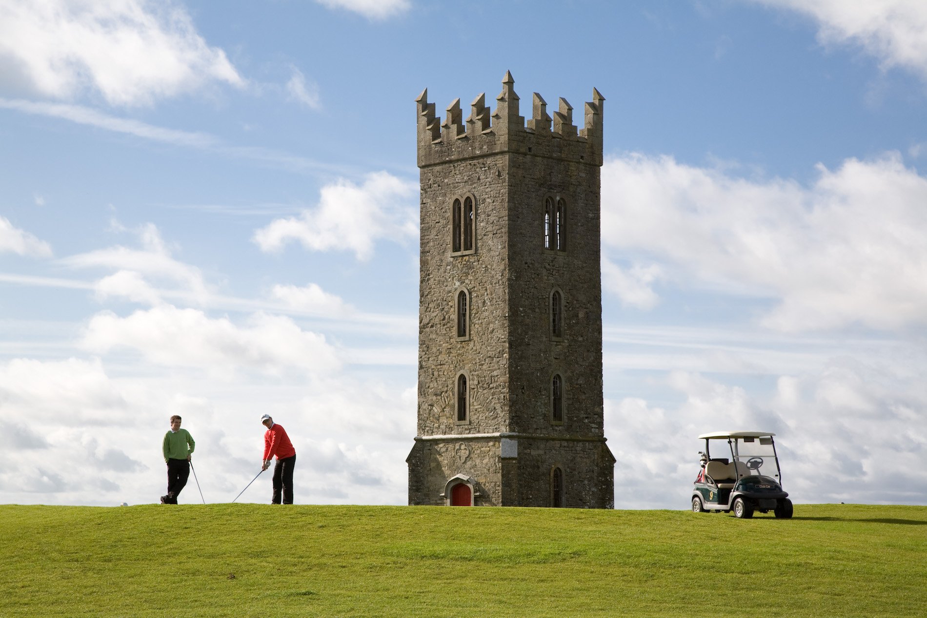 Carton House Golf Course, County Kildare, featuring a tall stone tower and golfers playing nearby.